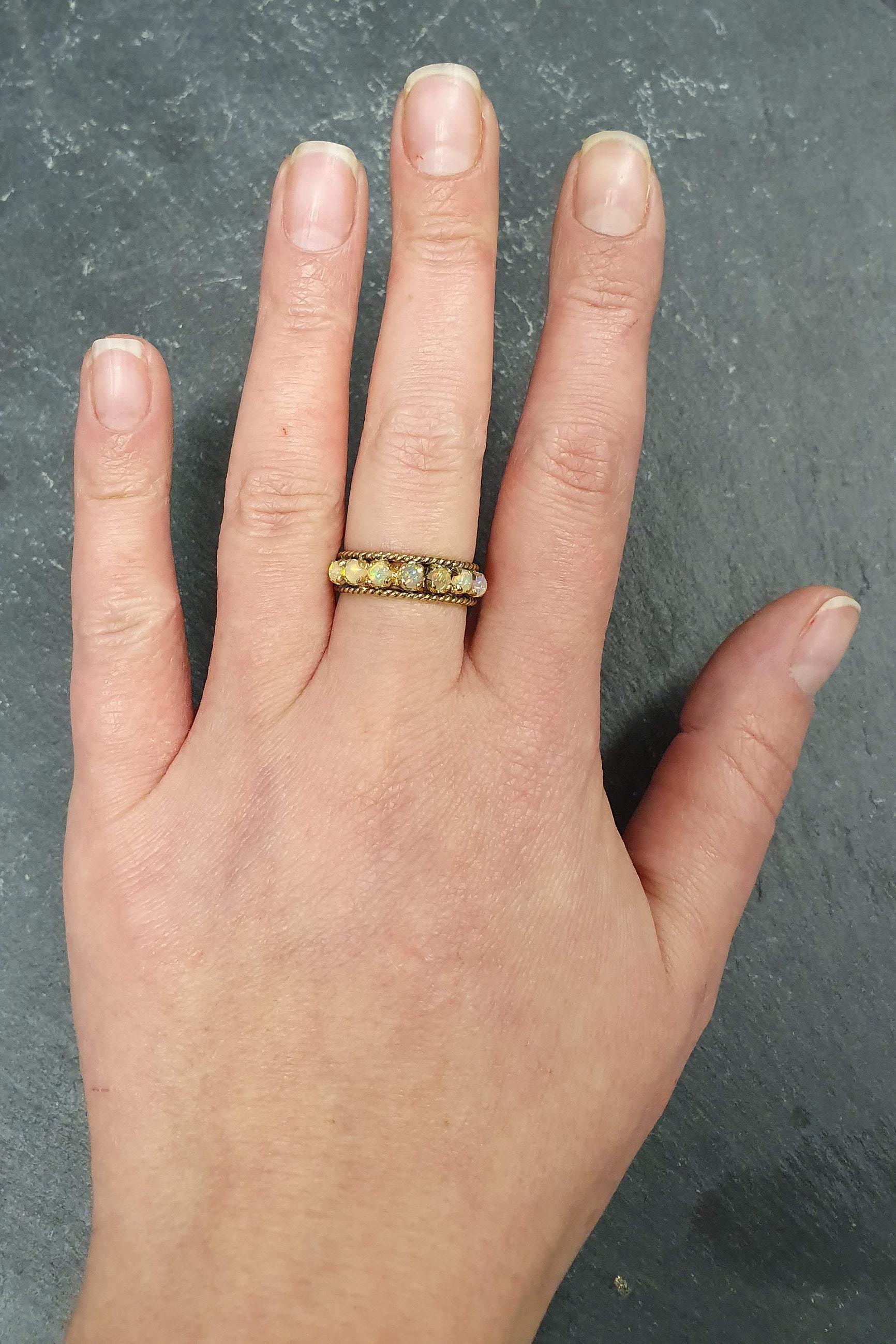 Opal Rope Row Ring styled on middle finger with bare nails, its cabochon opals shimmering with fire colors. A versatile October birthstone piece that enhances elegance, suitable for gifting loved ones, and perfect for casual brunches, birthdays, and celebratory occasions.