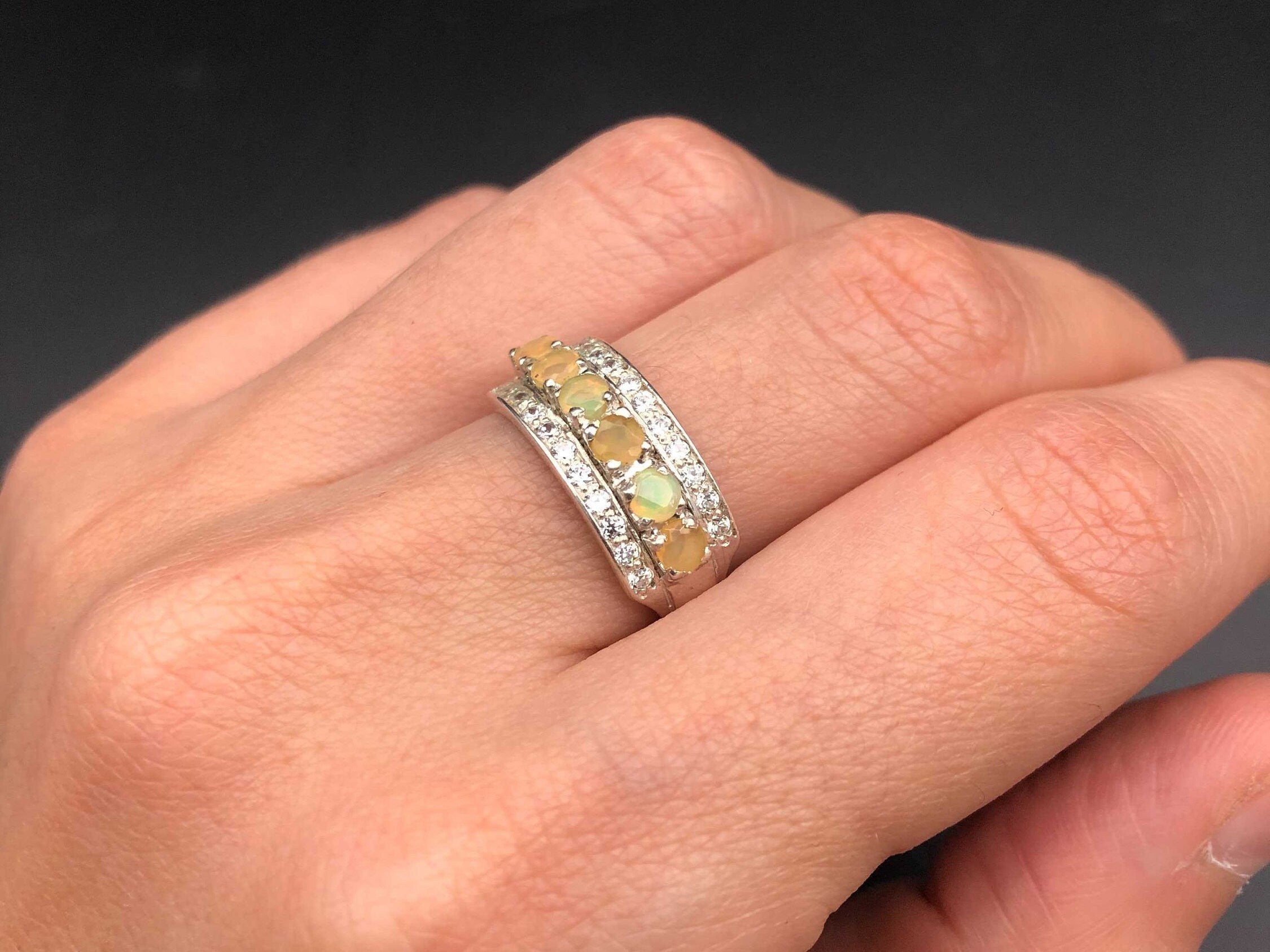 Opal Row Half Eternity Wide Ring worn on index finger with bare nails, its row of opals glowing with flashes of fire colors set between CZ pave bands. A striking October birthstone piece that enhances confidence and elegance, perfect for dinner dates, anniversaries, and celebratory gatherings.