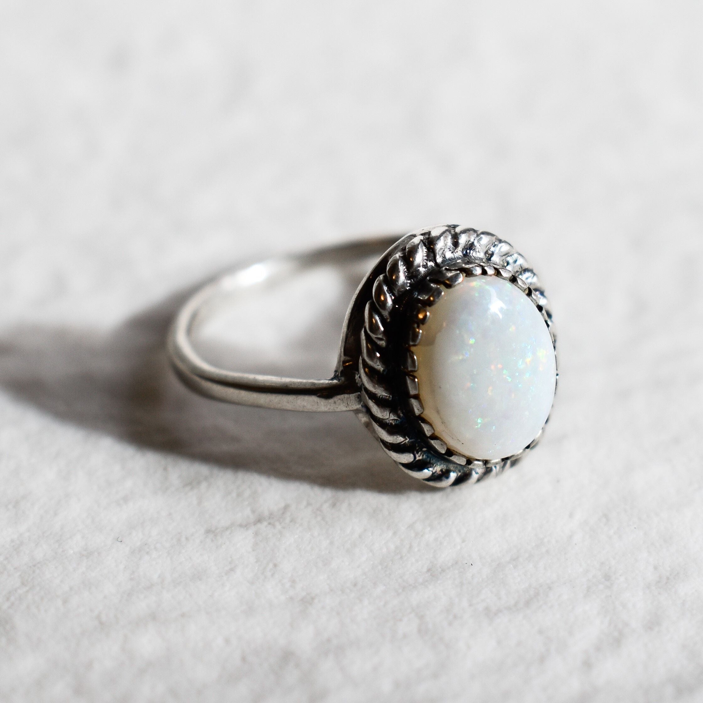 Natural Australian Opal sterling silver ring with an oval cabochon cut gemstone framed by a detailed rope-edge design, offering a timeless and elegant style. Opal, the October birthstone, is valued for enhancing creativity and emotional harmony, making it an ideal gift for birthdays, anniversaries, weddings, and milestone celebrations.