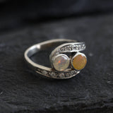 Two-Stone Opal Bypass Wave Ring in sterling silver showcasing cabochon-cut opals with flashes of fire colors and CZ pave accents for an elegant jewelry style. Known for enhancing emotional clarity and balance, this October birthstone ring makes a thoughtful and meaningful gift idea. Perfect for anniversaries, weddings, cocktail events, and celebratory occasions where sophistication shines.