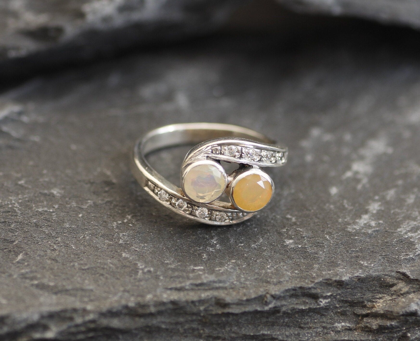 Two-Stone Opal Bypass Wave Ring in sterling silver showcasing cabochon-cut opals with flashes of fire colors and CZ pave accents for an elegant jewelry style. Known for enhancing emotional clarity and balance, this October birthstone ring makes a thoughtful and meaningful gift idea. Perfect for anniversaries, weddings, cocktail events, and celebratory occasions where sophistication shines.