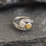 Two-Stone Opal Bypass Wave Ring in sterling silver showcasing cabochon-cut opals with flashes of fire colors and CZ pave accents for an elegant jewelry style. Known for enhancing emotional clarity and balance, this October birthstone ring makes a thoughtful and meaningful gift idea. Perfect for anniversaries, weddings, cocktail events, and celebratory occasions where sophistication shines.