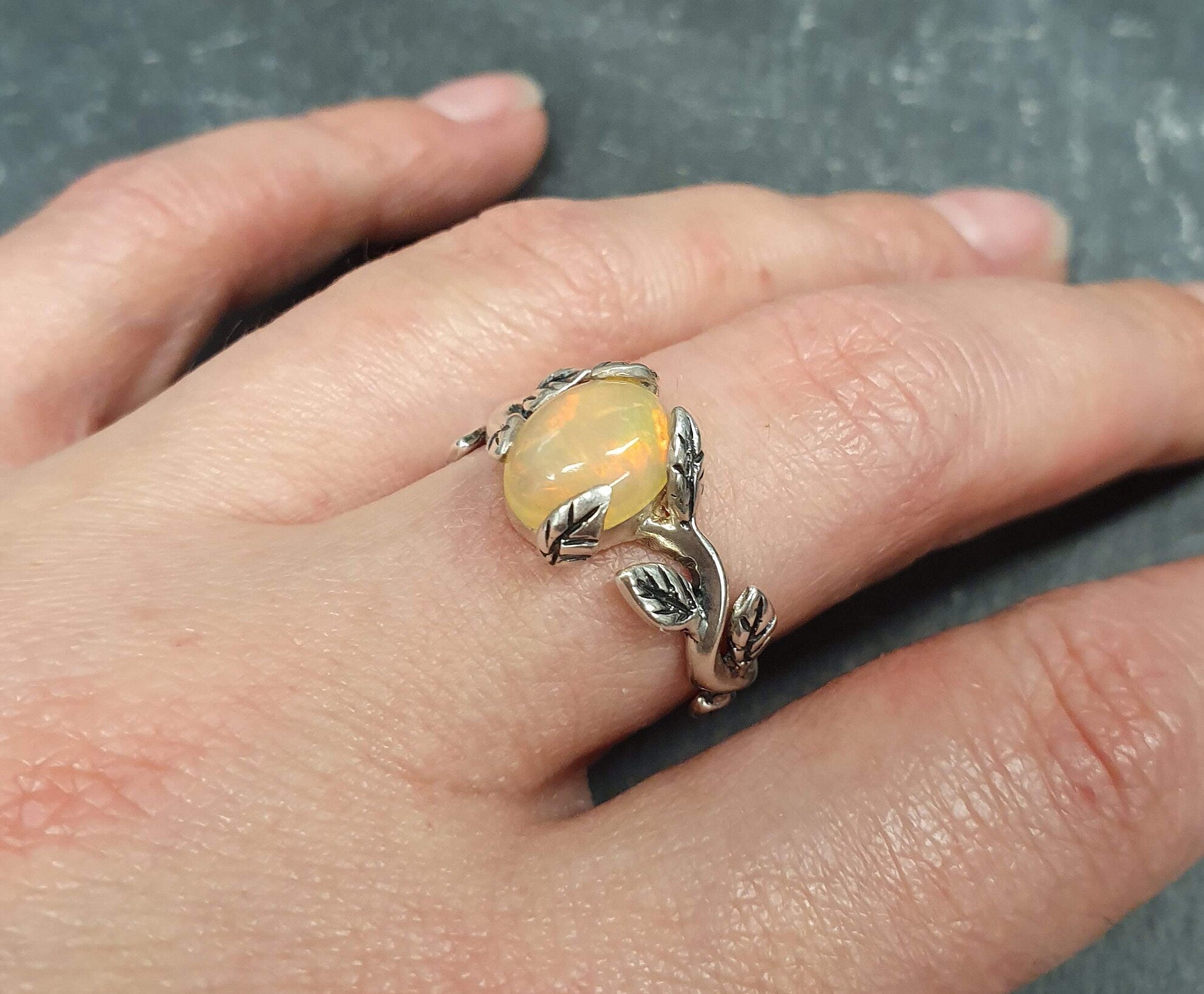 Flower Opal Ring worn on middle finger with bare nails, highlighting its vine and leaf design, perfect for adding a touch of boho nature charm, meaningful as an October birthstone gift, ideal for brunch outings and casual day events.