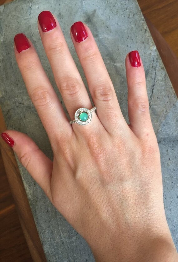 Emerald Halo Ring worn on the index finger with glossy red nails, sterling silver band accented with CZ stones highlighting the central opal’s flashes of fire colors. A chic October Birthstone design perfect for evening parties, romantic dinners, and wedding receptions.
