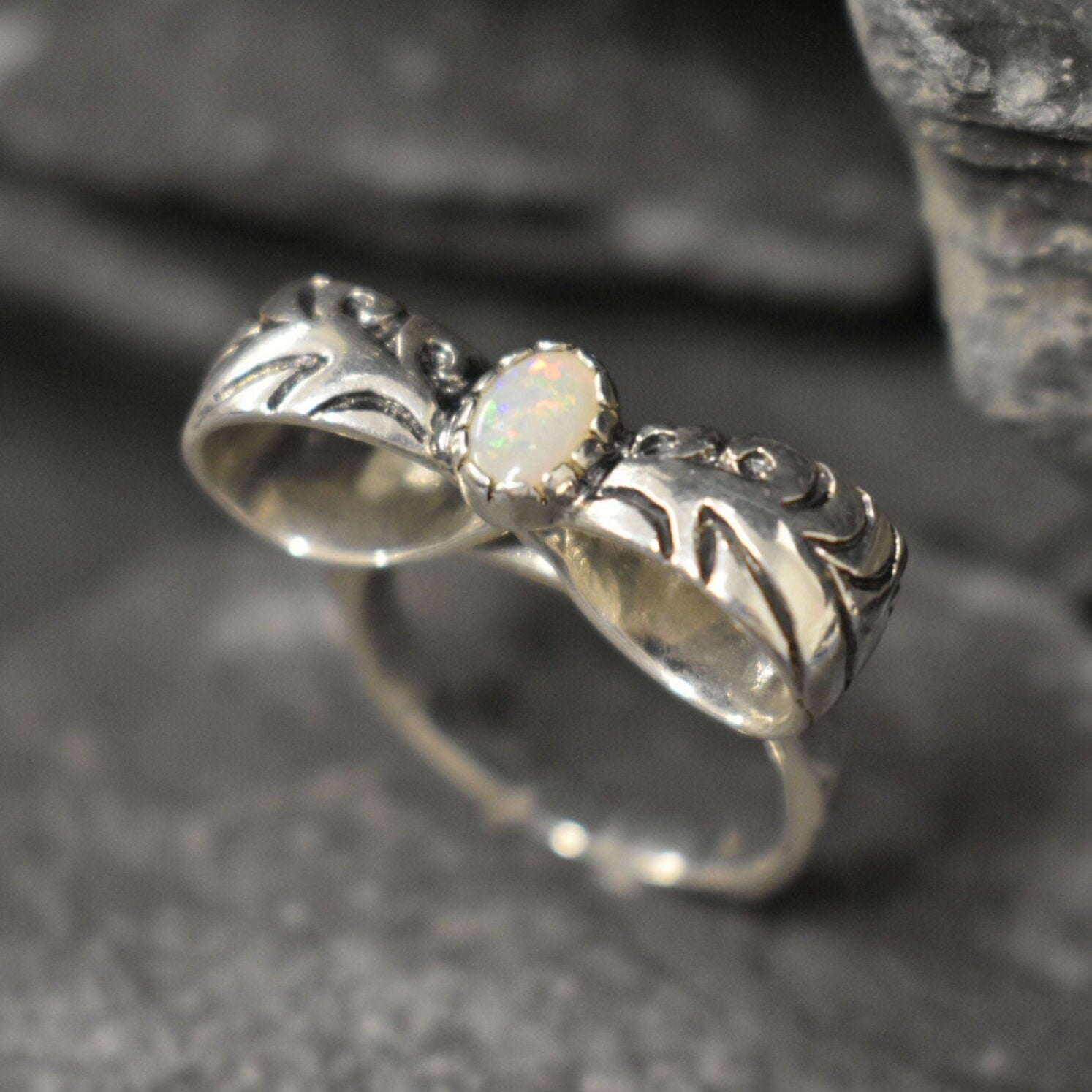 Opal ring in handcrafted solid silver with a ribbon bow style band and white cabochon showing flashes of fire color, a statement design that brightens the hand. Brings creative spark and calm confidence while adding a luminous white accent to any look. A thoughtful October birthstone gift idea for someone special.
Wear to weddings, anniversaries, engagements, date nights, office parties, graduations, and holiday gatherings.