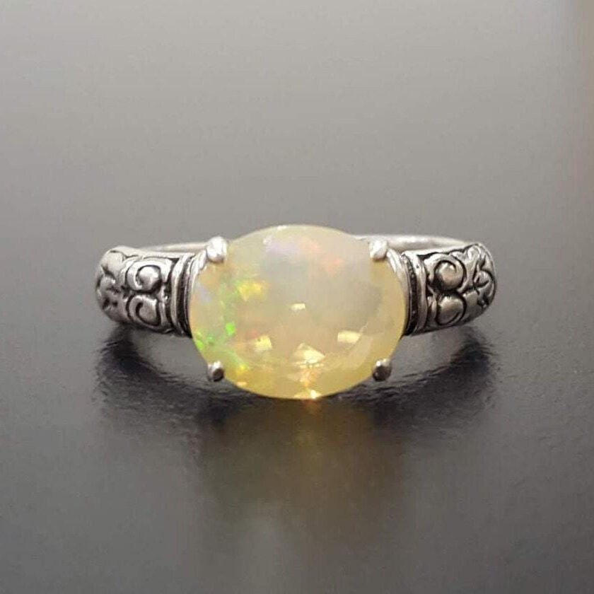 Ethiopian Fire Opal Sterling Silver Ring featuring a horizontal oval cut with a secure 4-prong setting. The engraved ornament band adds vintage charm, while the opal displays brilliant flashes of fire colors. A timeless October birthstone ring, perfect for birthdays, anniversaries, weddings, and milestone celebrations.