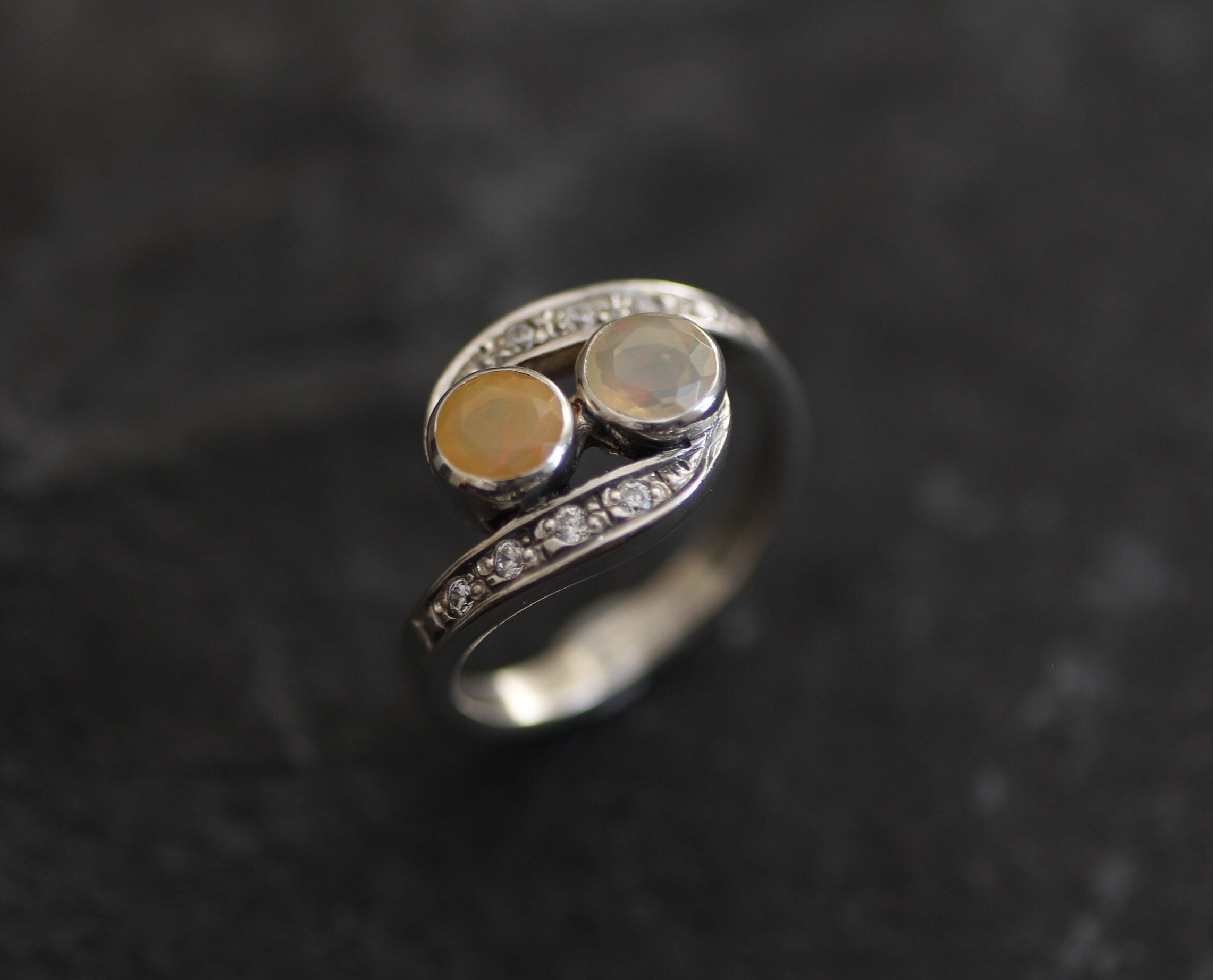 Two-Stone Opal Bypass Wave Ring in sterling silver showcasing cabochon-cut opals with flashes of fire colors and CZ pave accents for an elegant jewelry style. Known for enhancing emotional clarity and balance, this October birthstone ring makes a thoughtful and meaningful gift idea. Perfect for anniversaries, weddings, cocktail events, and celebratory occasions where sophistication shines.