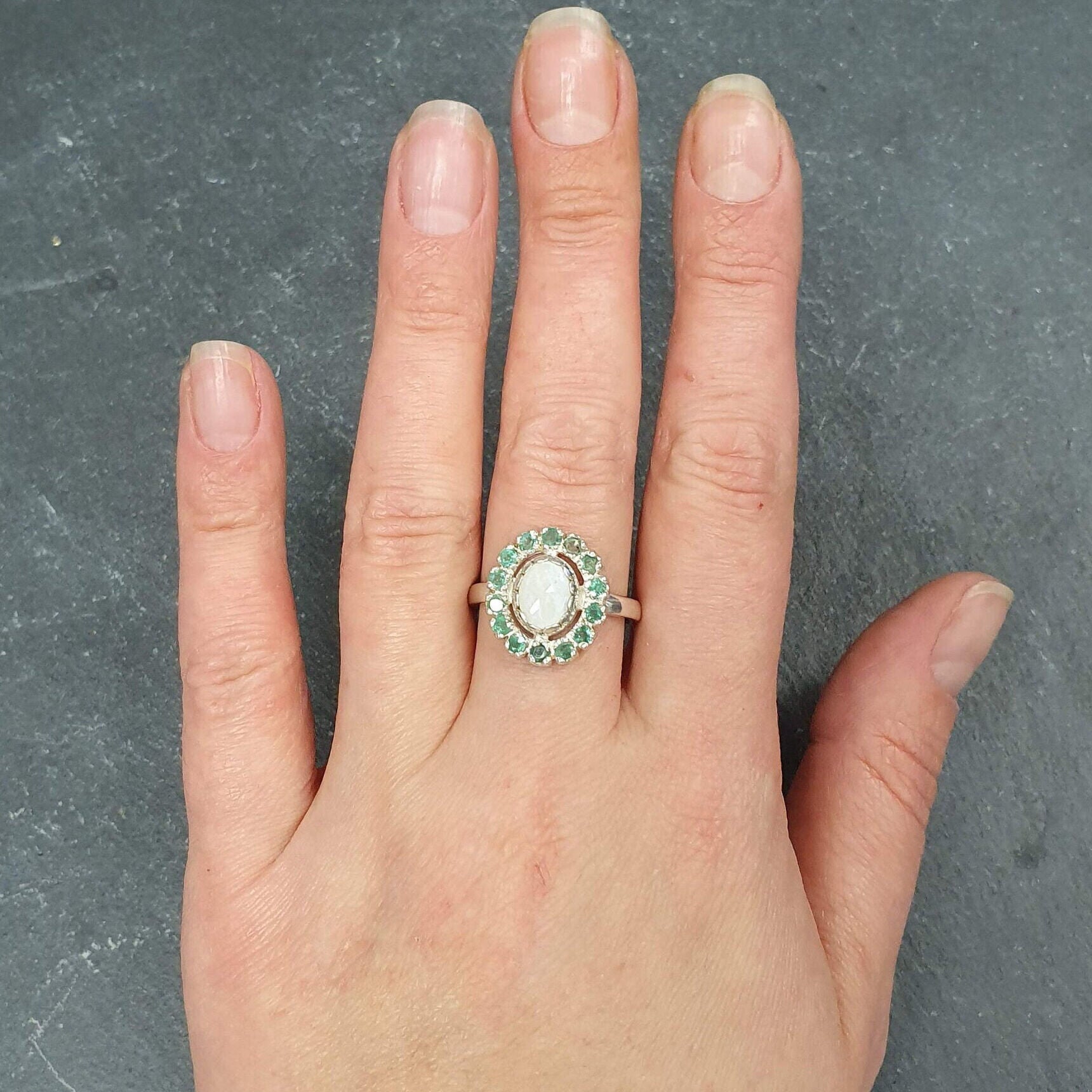 Sterling Silver Opal and Emerald Halo Ring worn with neutral manicure, perfect for adding a sophisticated touch and believed to bring harmony and love, suitable for weddings and evening gatherings.