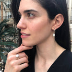 Opal Solitaire Ring styled with a black v-neck blouse and matching white opal drop earrings. Jewelry style is elegant and modern with a bezel design showing flashes of rainbow colors. Symbolizes creativity, harmony, and positivity. A meaningful October birthstone gift for birthdays or milestones. Ideal for evening dinners, weddings, and cocktail events.