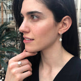 Opal Solitaire Ring styled with a black v-neck blouse and matching white opal drop earrings. Jewelry style is elegant and modern with a bezel design showing flashes of rainbow colors. Symbolizes creativity, harmony, and positivity. A meaningful October birthstone gift for birthdays or milestones. Ideal for evening dinners, weddings, and cocktail events.