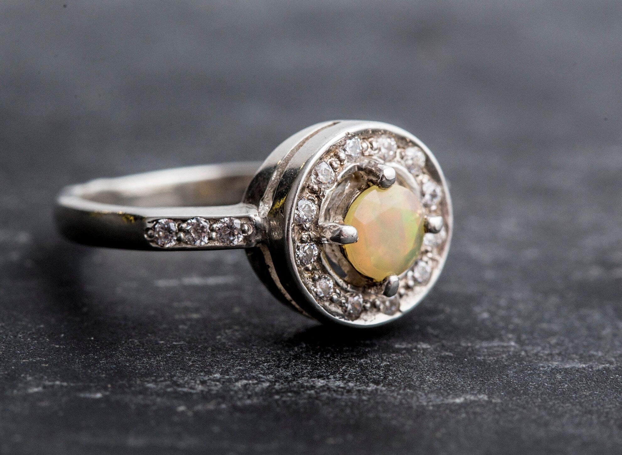 Ethiopian Opal diamond cut halo ring in solid 925 sterling silver, surrounded by sparkling CZ accents for brilliance and elegance. The halo design highlights flashes of fire colors while offering timeless durability. As the October Birthstone, Opal makes a meaningful gift for birthdays, engagements, anniversaries, or personal milestones. Perfect to wear at weddings, cocktail parties, and festive gatherings.