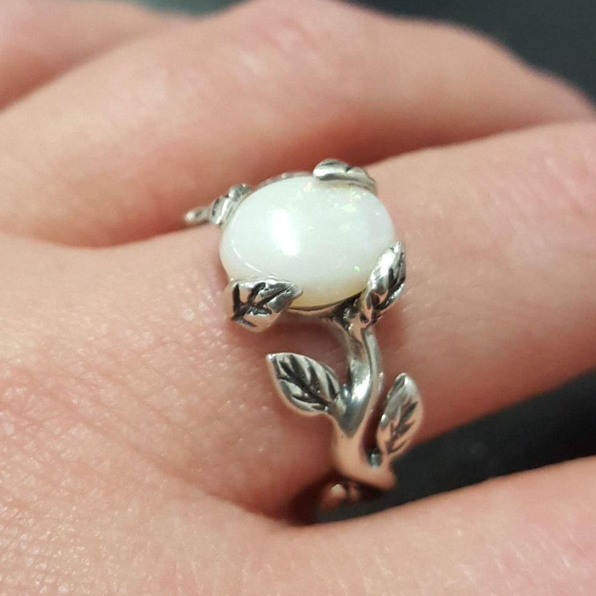 White Opal Ring worn on the middle finger with natural nails, leaf accents surrounding the glowing cabochon for a delicate nature-inspired look. A symbolic October Birthstone design perfect for weddings, evening events, and festive gatherings