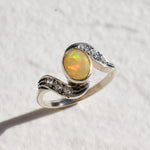 Bezel set vintage opal ring in a gold wave design with flashes of rainbow and fire colors, accented by sparkling stones on each curve. Opal is believed to inspire creativity, hope and emotional balance, making it a meaningful October birthstone gift for anniversaries, engagements, weddings and special celebrations.