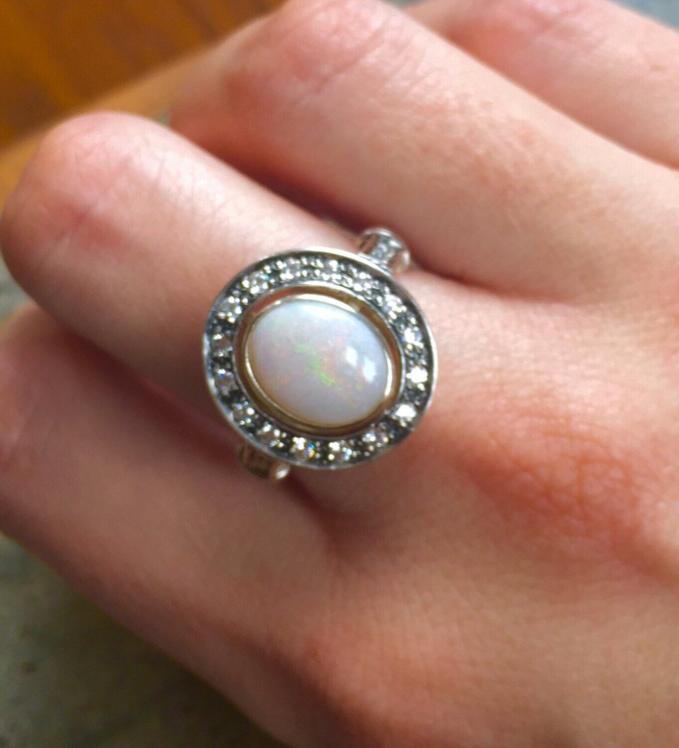 Opal Bezel Halo Ring worn on Middle  finger, showcasing an oval opal with rainbow and fire colors surrounded by CZ diamonds. Perfect for special occasions, weddings and cocktail parties. Ideal gift for October babies.