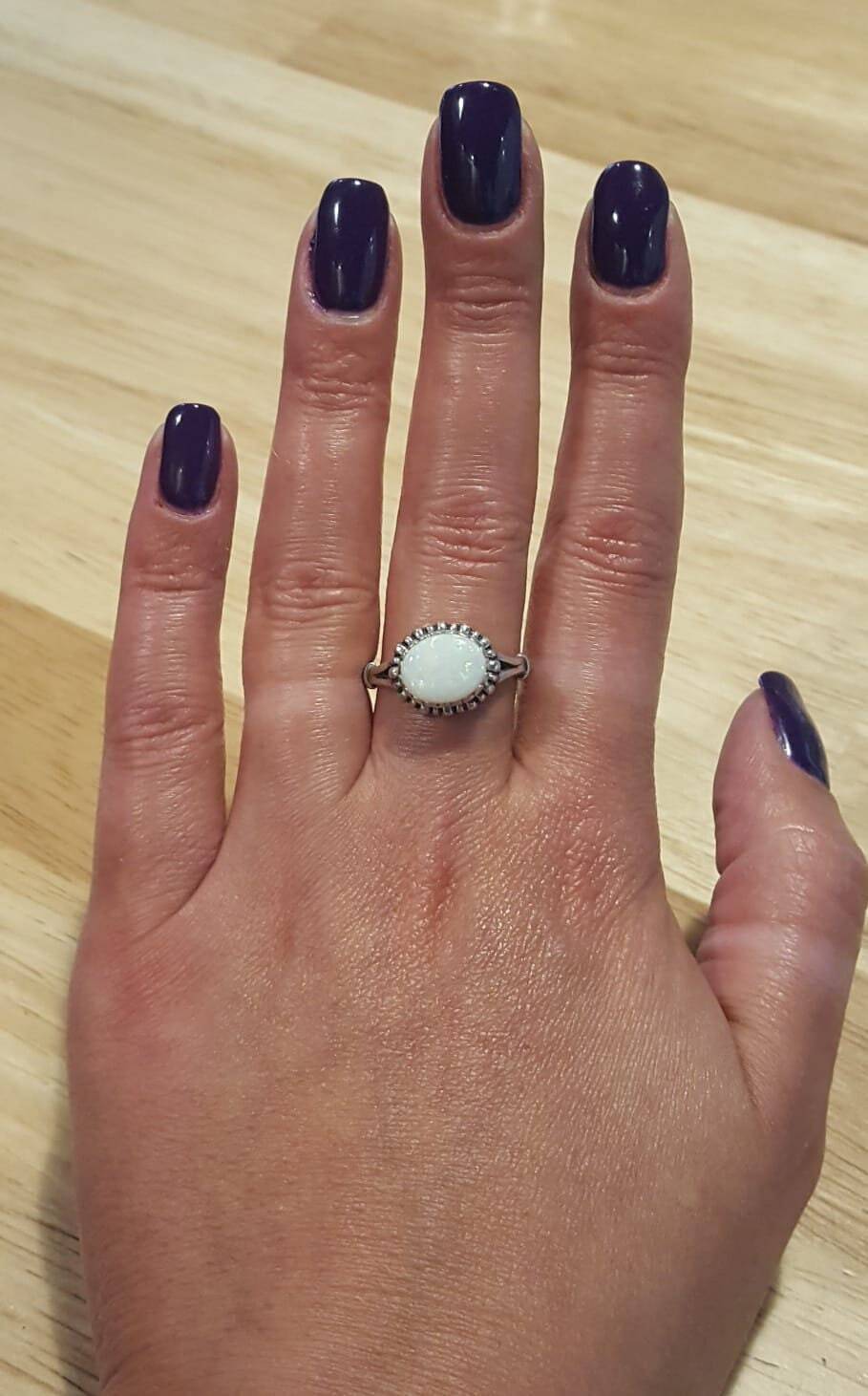 White Fire Opal Ring worn on middle finger with purple  nails, horizontal cabochon design shimmering with flashes of fire colors, meaningful October birthstone jewelry. Perfect for weddings, anniversaries, and elegant celebrations.
