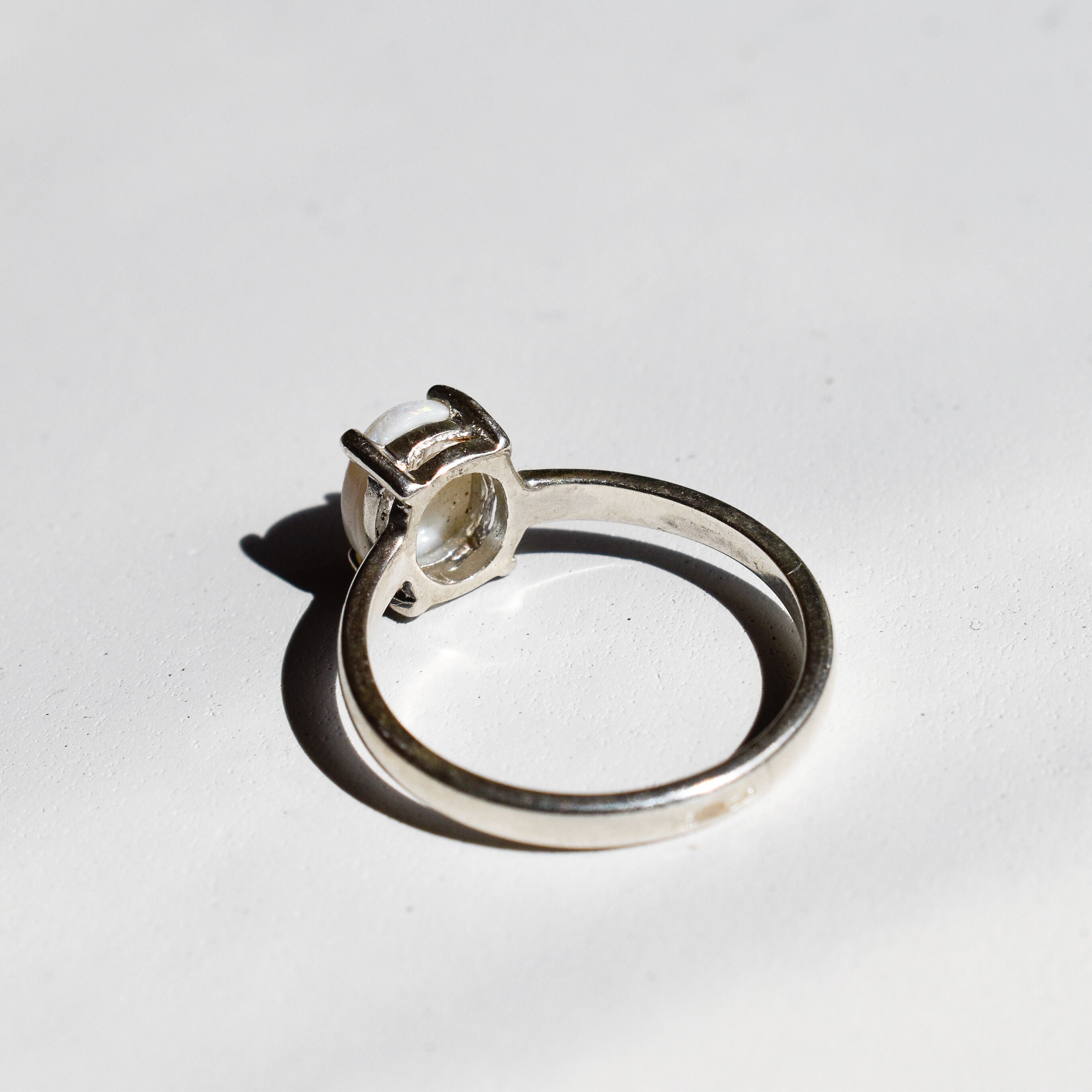 White Opal solitaire ring in sterling silver showcasing flashes of rainbow colors, dainty jewelry style perfect for daily elegance, believed to bring inspiration and emotional balance, a meaningful October birthstone gift idea for anniversaries, engagements, and weddings.