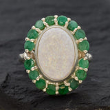 Opal and Emerald Large Cocktail Ring in sterling silver featuring an oval white opal cabochon framed with genuine emerald petals, a statement jewelry style that radiates flashes of fire colors while symbolizing love and renewal, making it a meaningful October and May birthstone gift idea. Perfect for weddings, cocktail parties, and formal evening events where a bold elegant look is desired.