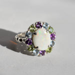 White Opal flower cluster ring in sterling silver with colorful Amethyst and Peridot halo in a cocktail style. The elegant cluster design adds sparkle. Opal is linked with hope and clarity, Amethyst with calm, Peridot with fresh energy. A lovely birthstone gift for October, February and August. Wear to weddings, graduations, dinner dates and holiday parties.