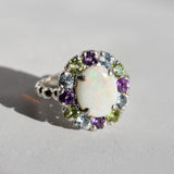 White Opal flower cluster ring in sterling silver with colorful Amethyst and Peridot halo in a cocktail style. The elegant cluster design adds sparkle. Opal is linked with hope and clarity, Amethyst with calm, Peridot with fresh energy. A lovely birthstone gift for October, February and August. Wear to weddings, graduations, dinner dates and holiday parties.