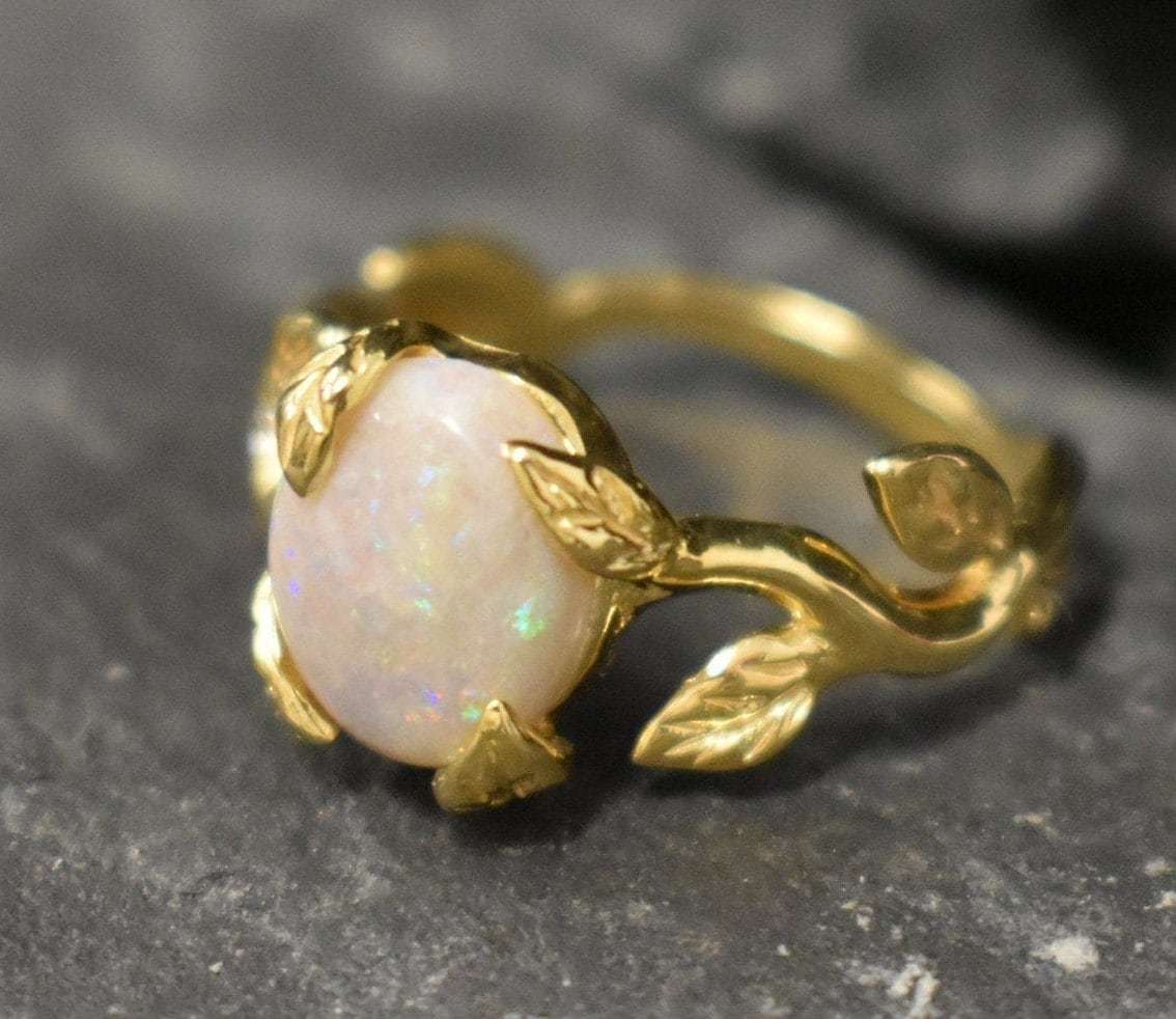 White Opal cabochon vine and leaf ring crafted in gold, featuring a nature-inspired design with flashes of fire colors. The durable vine-style band offers elegance and uniqueness while remaining comfortable for daily wear. As the October Birthstone, White Opal makes a thoughtful gift for birthdays, anniversaries, and nature lovers. Perfect to wear at weddings, outdoor celebrations, and festive gatherings.