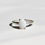 White Opal solitaire ring in sterling silver showcasing flashes of rainbow colors, dainty jewelry style perfect for daily elegance, believed to bring inspiration and emotional balance, a meaningful October birthstone gift idea for anniversaries, engagements, and weddings.