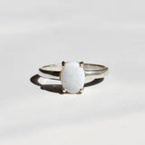 White Opal solitaire ring in sterling silver showcasing flashes of rainbow colors, dainty jewelry style perfect for daily elegance, believed to bring inspiration and emotional balance, a meaningful October birthstone gift idea for anniversaries, engagements, and weddings.