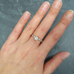 White Opal Ring worn on middle finger with natural bare nails, bezel solitaire style on twisted band for understated elegance, brings calm and positivity as an October birthstone, ideal for casual outings, coffee dates, or workdays.