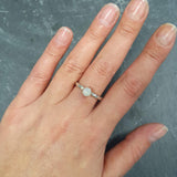 White Opal Ring worn on middle finger with natural bare nails, bezel solitaire style on twisted band for understated elegance, brings calm and positivity as an October birthstone, ideal for casual outings, coffee dates, or workdays.