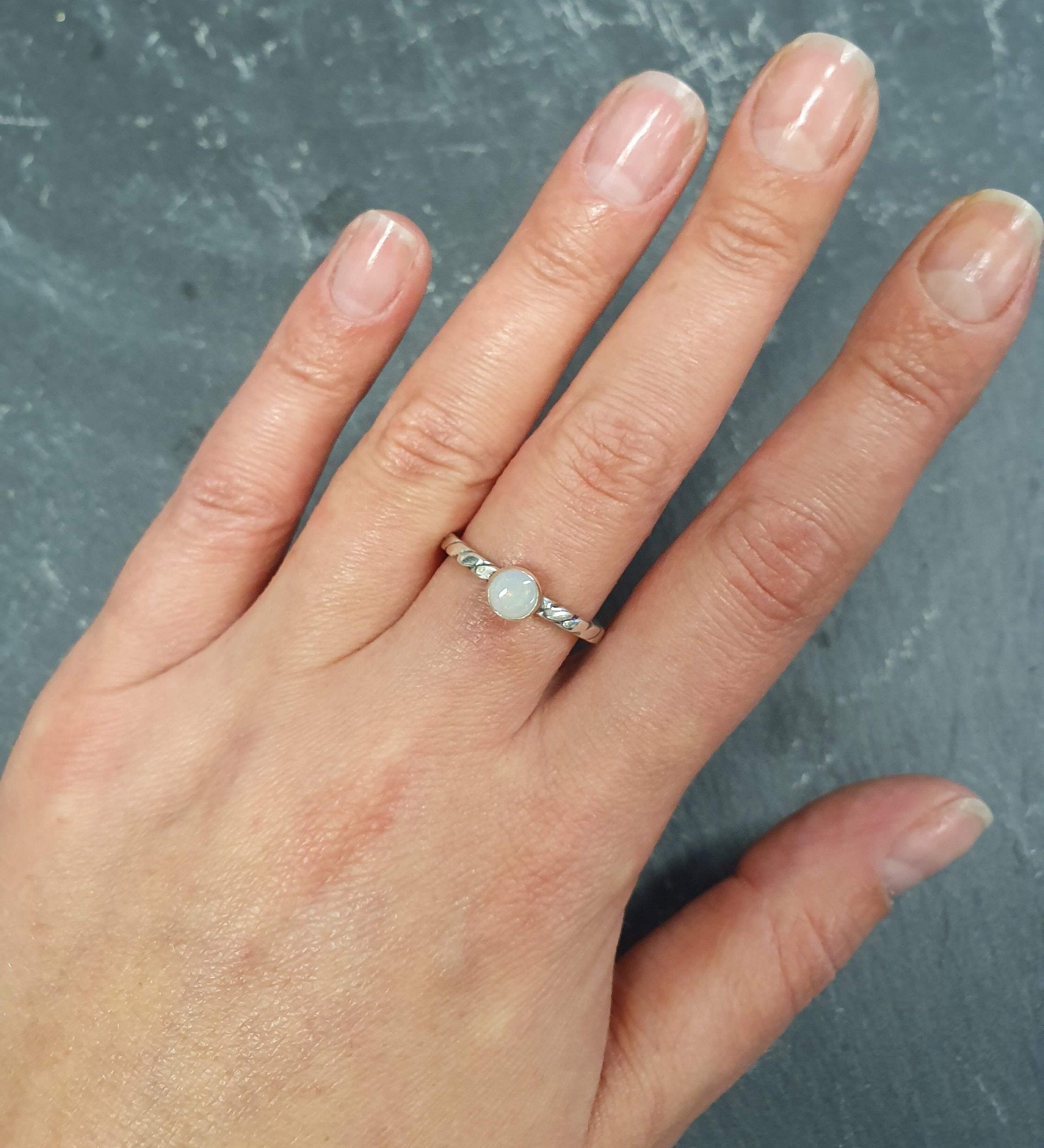 White Opal Ring worn on middle finger with natural bare nails, bezel solitaire style on twisted band for understated elegance, brings calm and positivity as an October birthstone, ideal for casual outings, coffee dates, or workdays.
