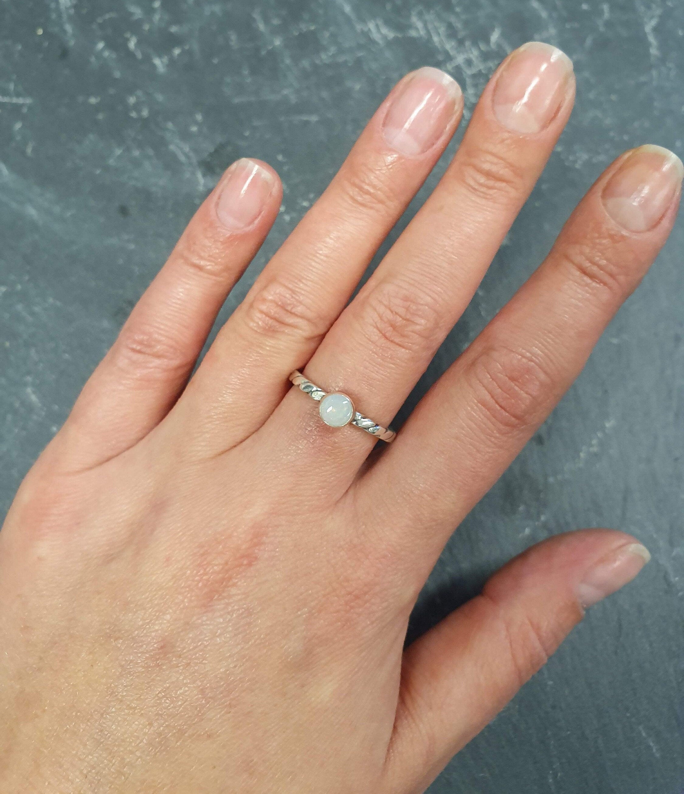 White Opal Ring worn on middle finger with natural bare nails, bezel solitaire style on twisted band for understated elegance, brings calm and positivity as an October birthstone, ideal for casual outings, coffee dates, or workdays.