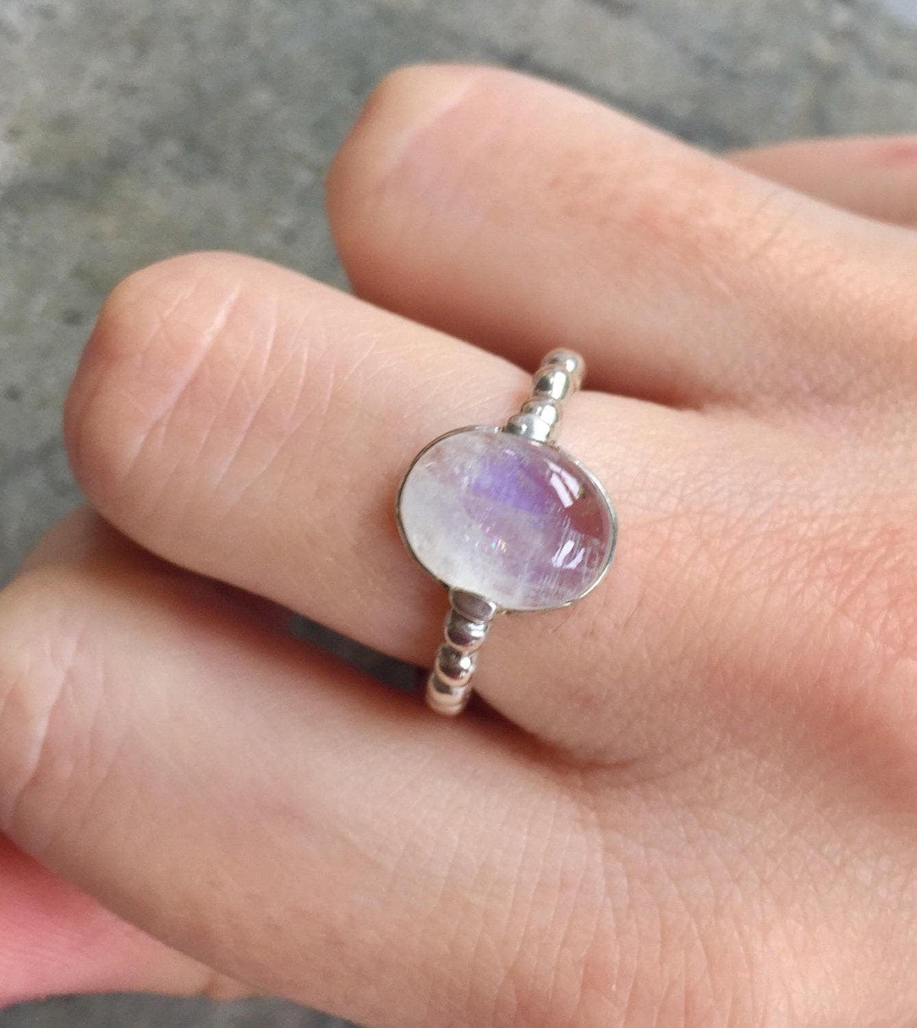 Moonstone ring with textured silver band worn on middle finger, captured in a soft-toned outfit with bare nails, adding calm and understated charm to everyday wear.