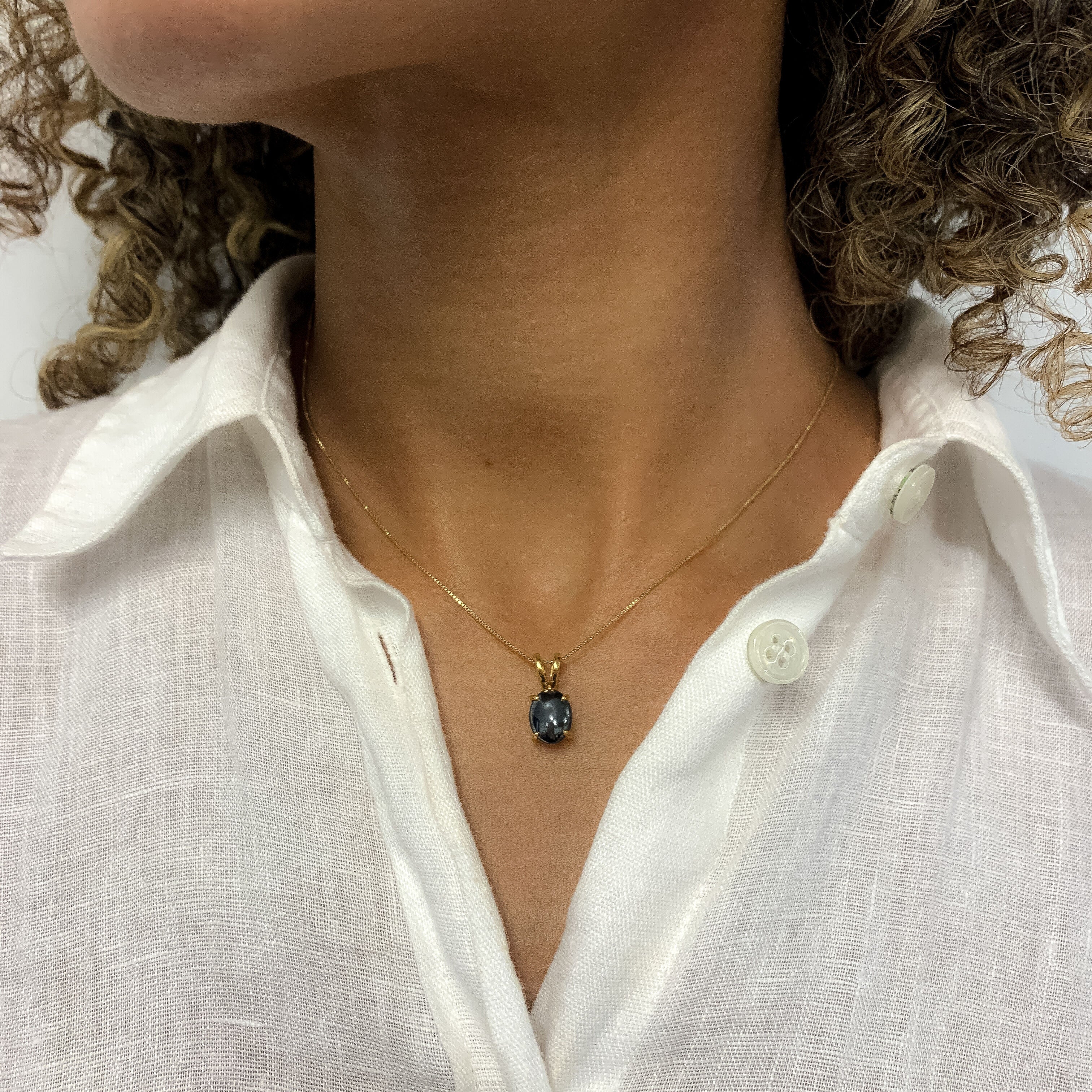 Woman in white linen shirt wearing natural black hematite necklace, set in gold vermeil over sterling silver. Black gemstone pendant that stands out and styles well with white and minimalist outfit. 