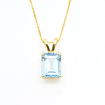 Blue topaz pendant with 10x8mm emerald cut gemstone set in polished gold, shown on white background