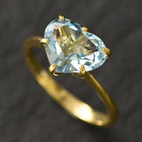 Close-up of blue topaz heart gold ring highlighting diamond-cut gemstone on dark background