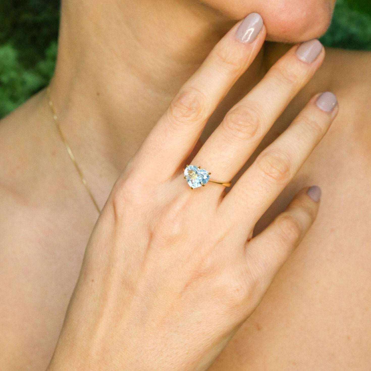 Woman wearing blue topaz heart gold ring showing sparkling gemstone and elegant gold band