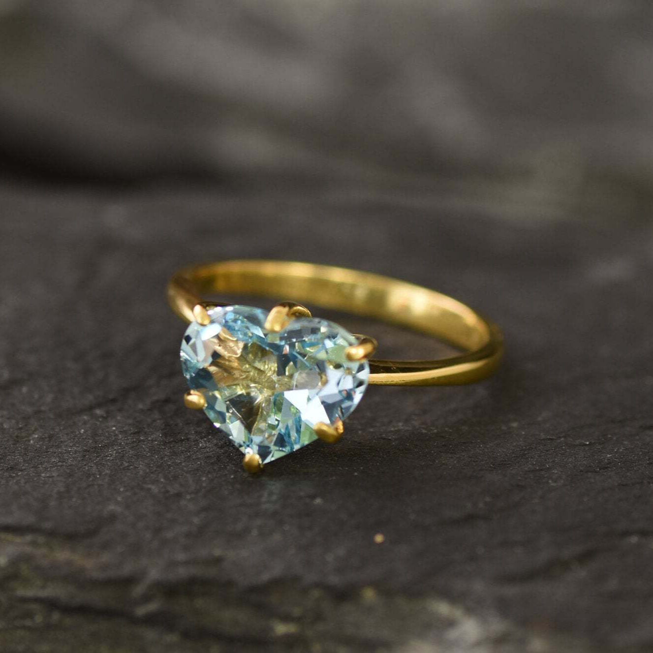 Front view of blue topaz heart gold ring showing vivid gemstone clarity on dark surface