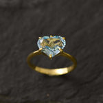 Side-angle close-up of blue topaz heart gold ring displaying gemstone details on dark surface