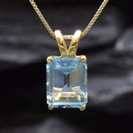 Close-up of blue topaz gemstone in emerald cut, set in gold with detailed prong setting