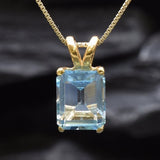 Close-up of blue topaz gemstone in emerald cut, set in gold with detailed prong setting