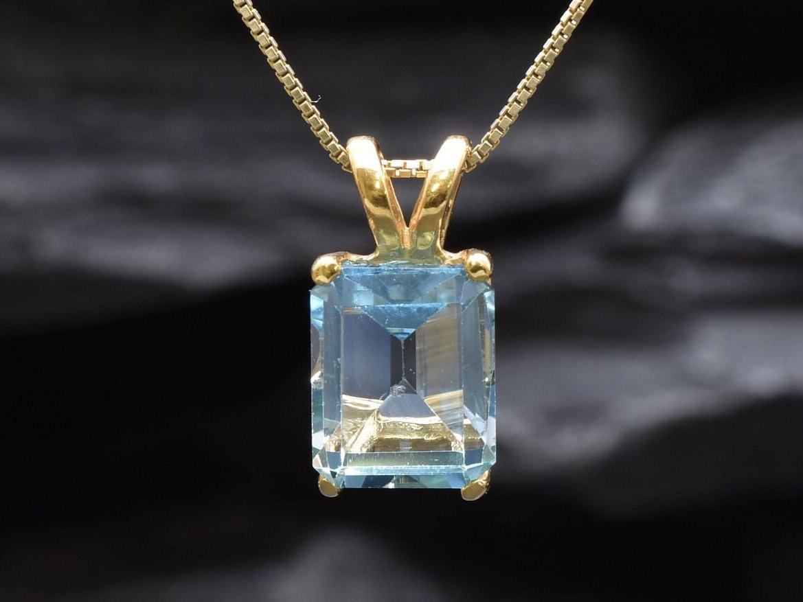 Close-up of blue topaz gemstone in emerald cut, set in gold with detailed prong setting