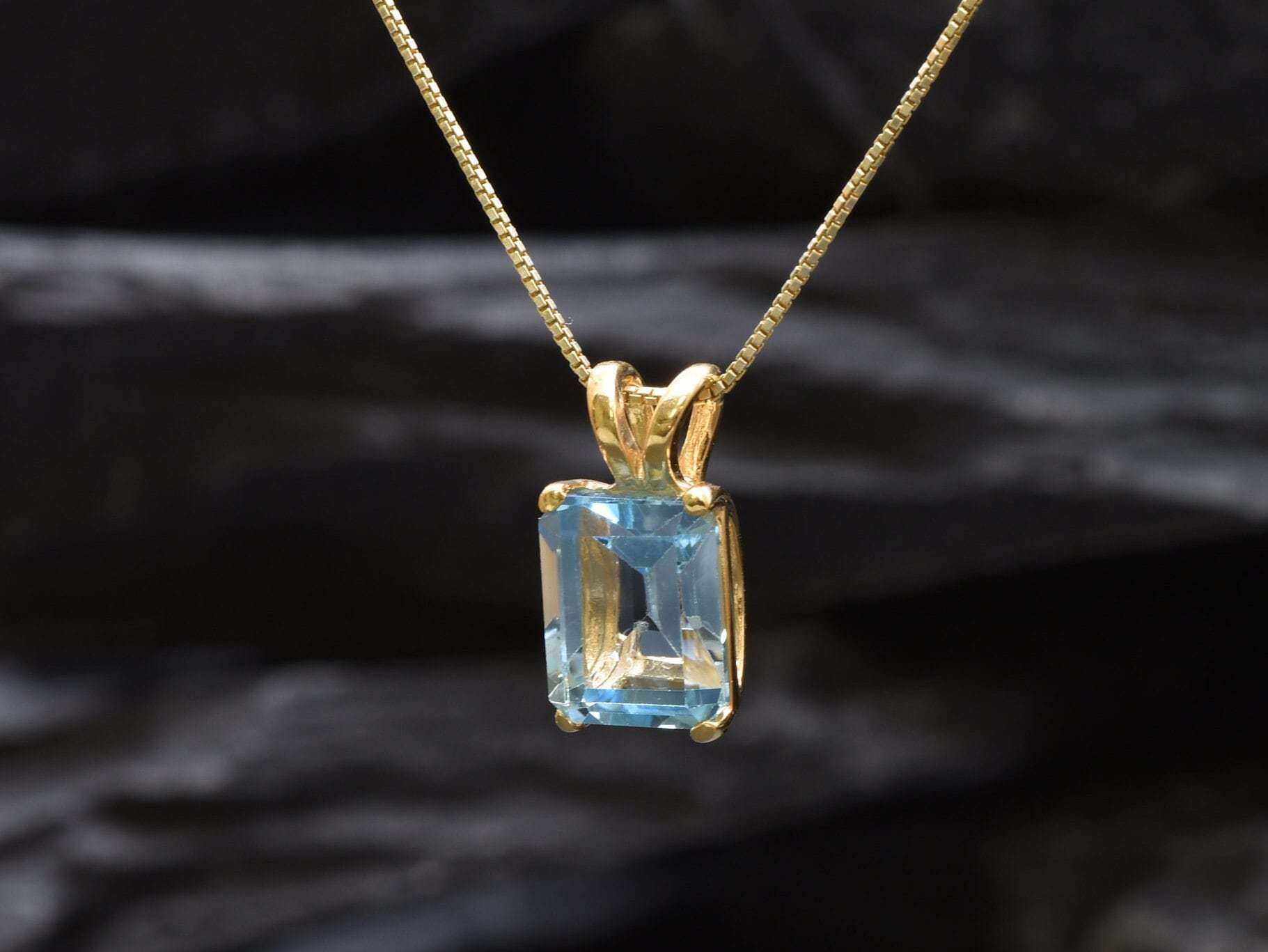 Flatlay of gold blue topaz pendant on dark background showing clean setting and bail detail