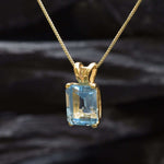 Flatlay of gold blue topaz pendant on dark background showing clean setting and bail detail