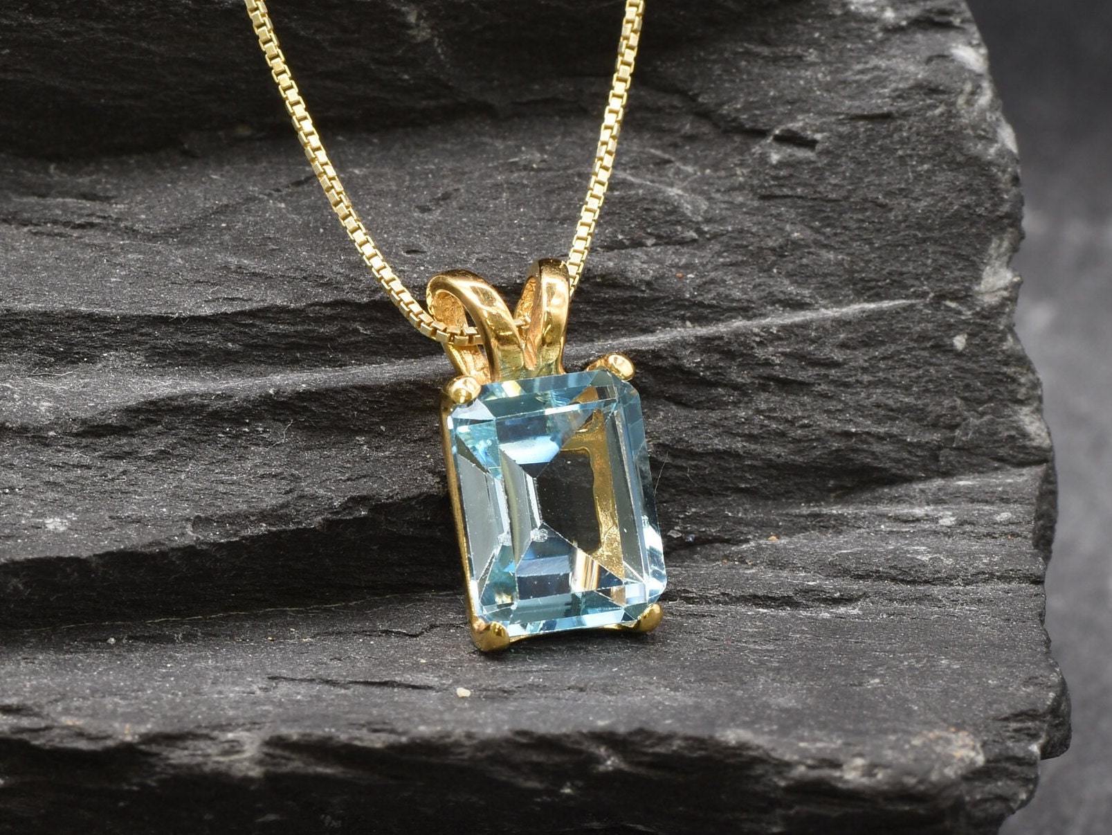 Flatlay of gold blue topaz pendant on dark background showing clean setting and bail detail