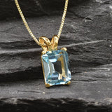 Flatlay of gold blue topaz pendant on dark background showing clean setting and bail detail
