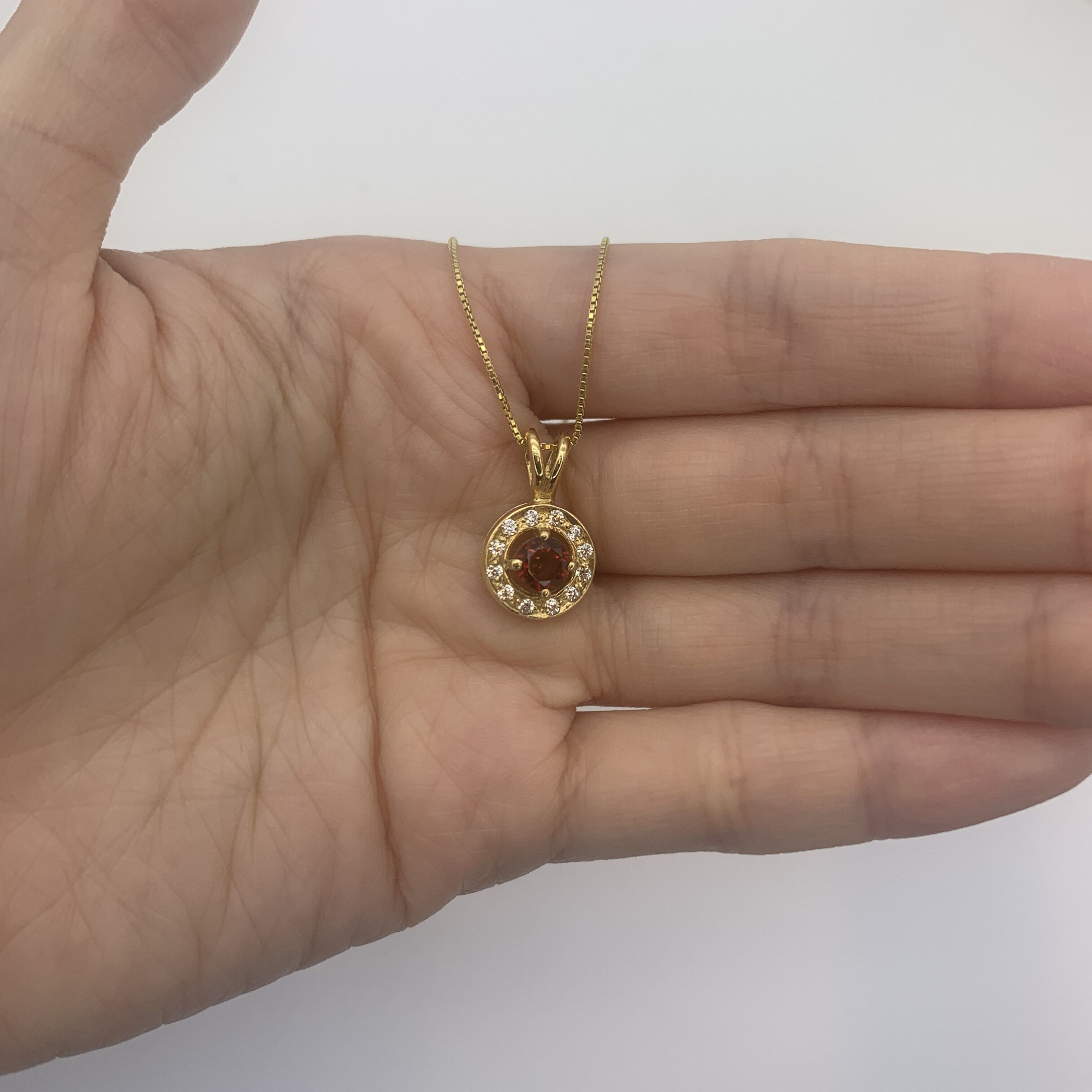 Dainty gold halo pendant with natural garnet January birthstone shown in a hand for scale – handcrafted red gemstone necklace