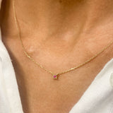 Woman in white top wearing a natural July birthstone Ruby necklace in solid 14k yellow gold chain. In a prong setting, and natural red color. Best worn in a minimalist look, can be worn as an everyday necklace