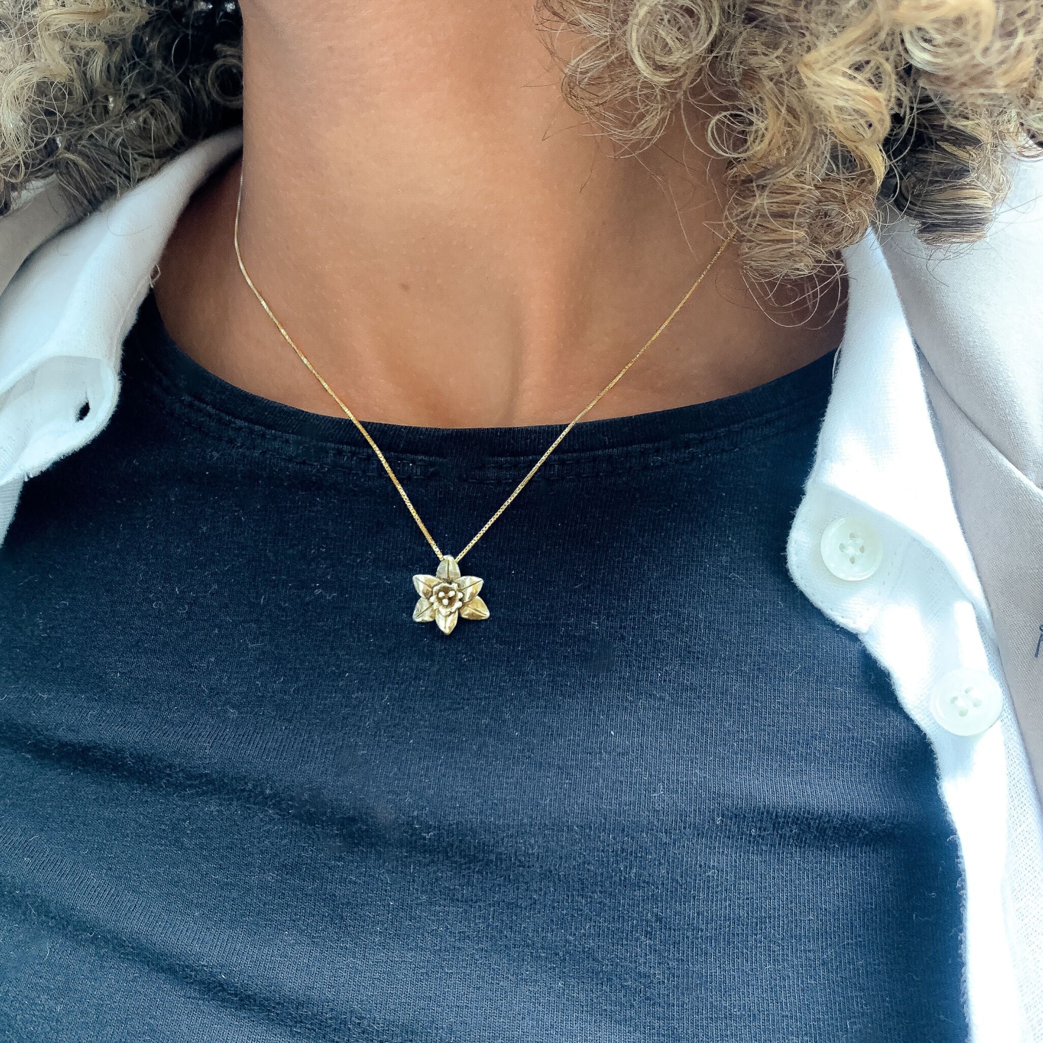 Woman wearing 18k yellow gold plated necklace with poinsettia flower design. Dainty floral pendant ideal as personalized gift, and good for layering necklaces. Gold charm pendant for everyday wear.