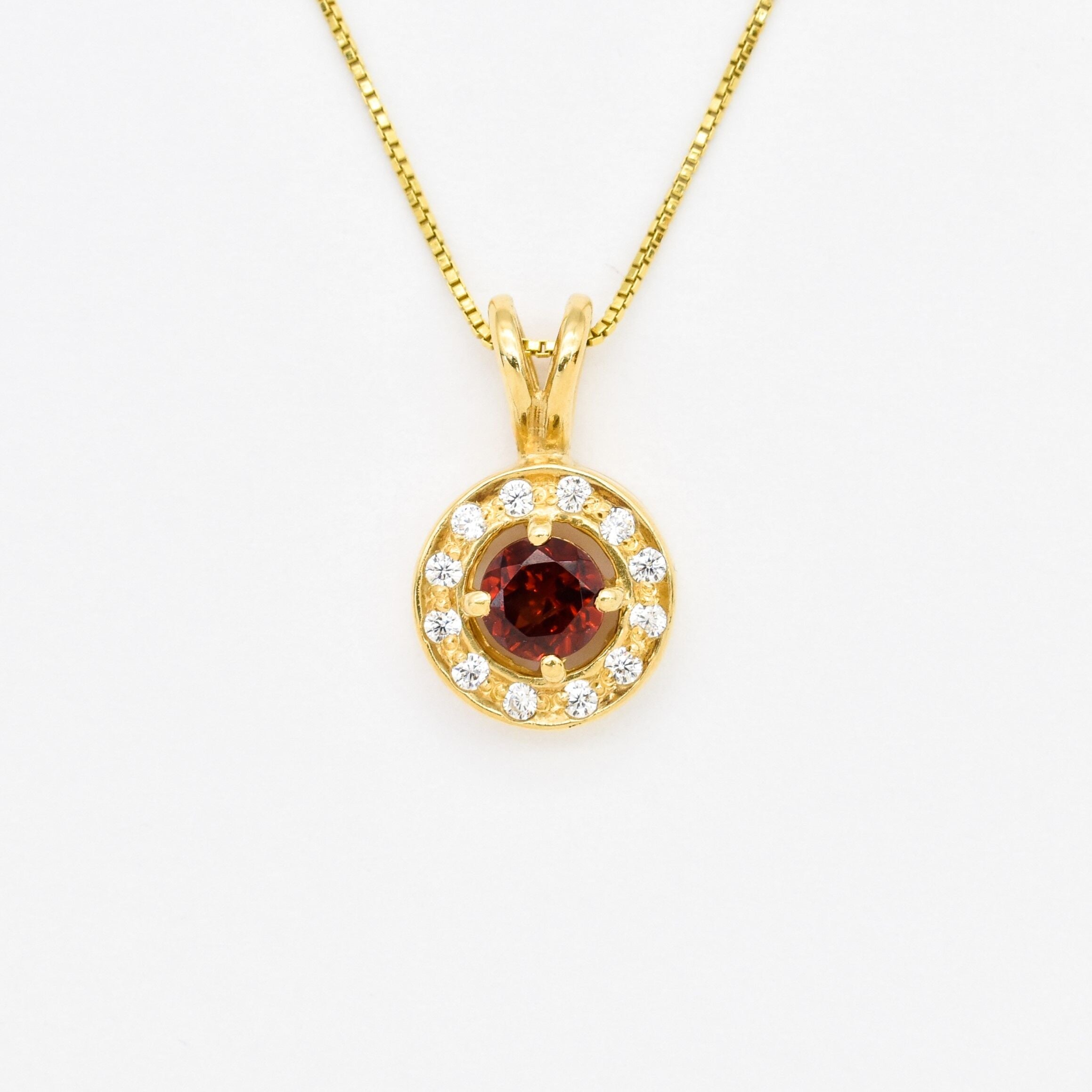 Natural Garnet January birthstone necklace crafted in 18k yellow gold over sterling silver, in round cut and prong setting, surrounded with small CZ diamonds. Dainty red garnet pendant that boosts confidence, enhances courage, and inspires love and success. For passion, protection, & vitality.