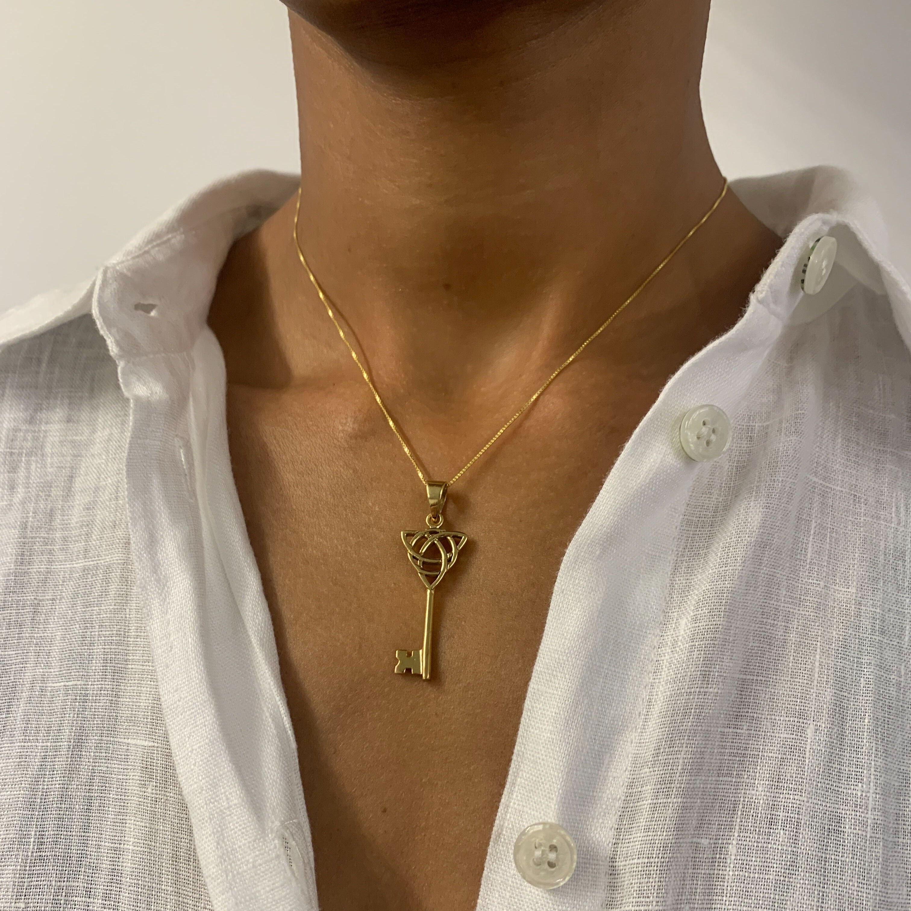 Woman in white linen shirt wearing Long Key Pendant set in 18k Yellow Gold Vermeil over Solid 925 Sterling Silver. Gold Key Necklace with Trinity Know, perfect as a statement necklace, can be styled with minimalist outfit.  Trinity knot represents unity, eternal love, and the cycle of existence.