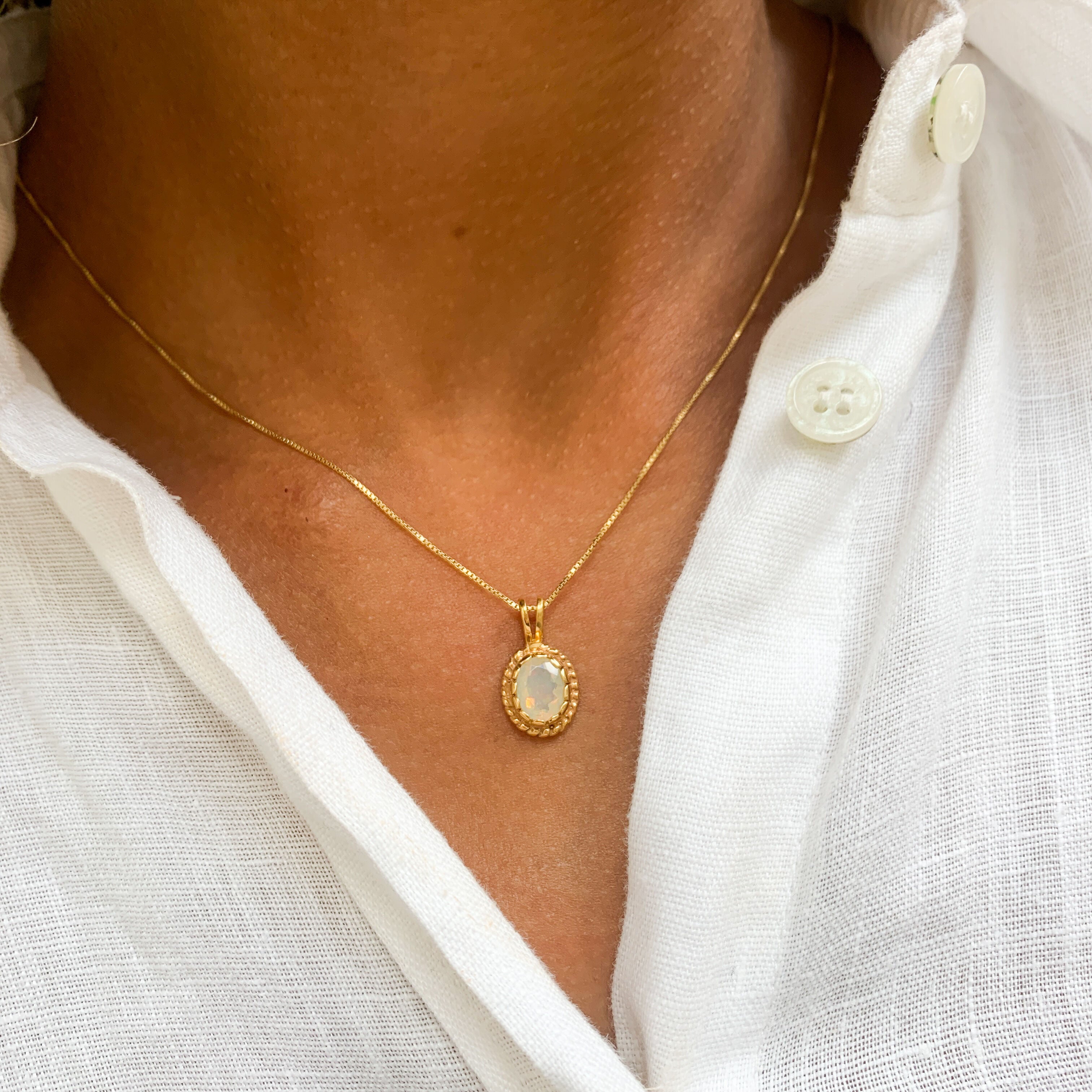 Woman in a white linen shirt, wearing natural opal pendant set in 18k yellow gold over sterling silver. Fire opal necklace ideal gift for her, perfect for wearing solo, and layering necklaces. 